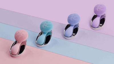 Electric face washer in various colors: pink, blue, and purple against a pastel background